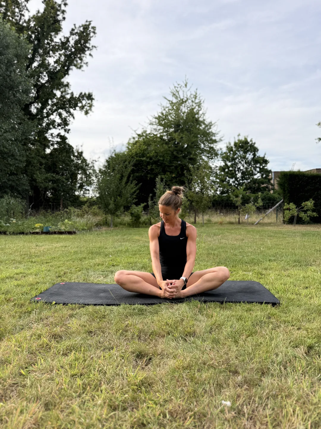 Fie zit buiten op haar Pilatesmat in een vlinderstretch